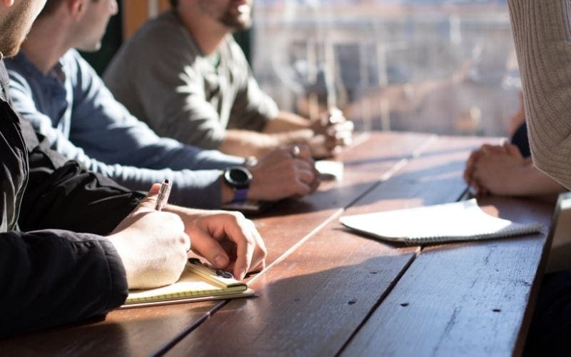 Men sat at a wooden desk with pen paper and smart watched on a Music Publisher search