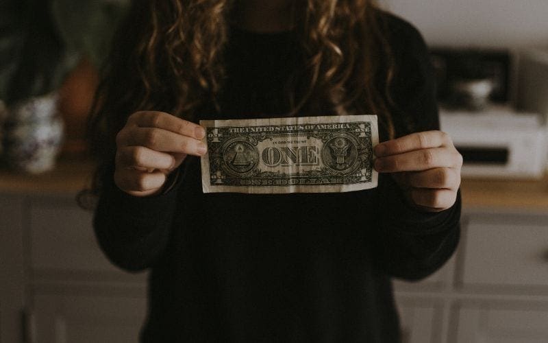 A girl with long curly hair holding a dollar she earned from a music publishing company