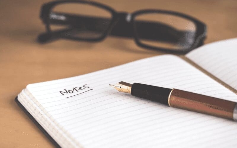 Notepad that says Notes, next to pen and glasses.