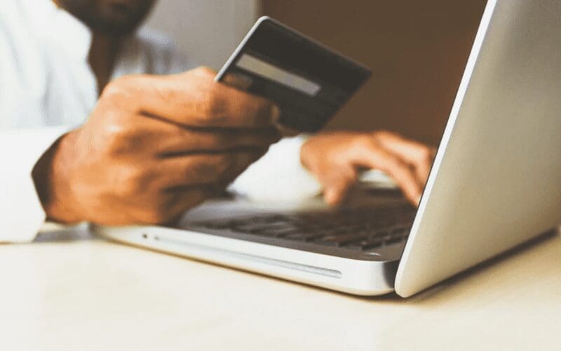 A business man holding a credit card while on the laptop. 
