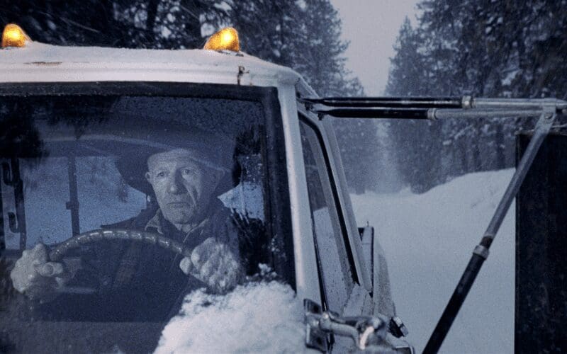 Old man driving his car in the snow.
